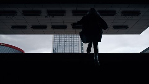 Silhouette woman walking up on stairs from subway or underground parking lot. Unknown female person going out metro station in daylight urban area. Walking and underground city concept. 