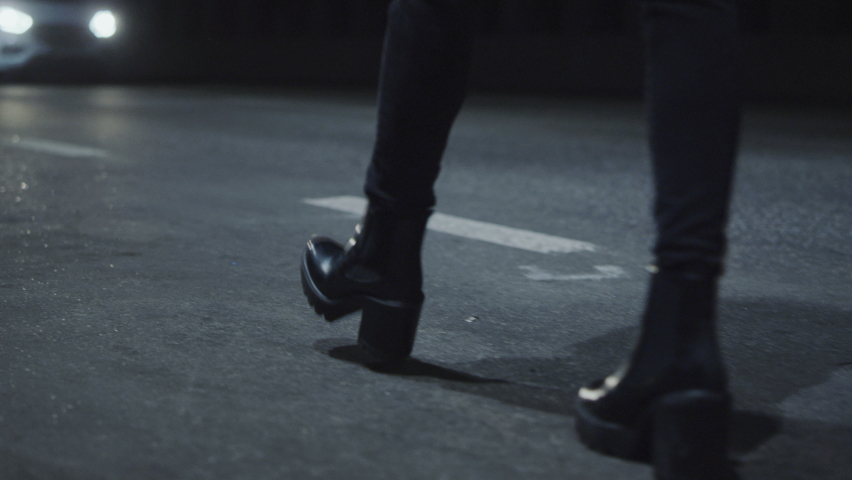 Woman shoes walking on dark road in driving tunnel at late night. Cars driving on night highway while female person legs going in high heel shoes at city night lights. Walking concept. 