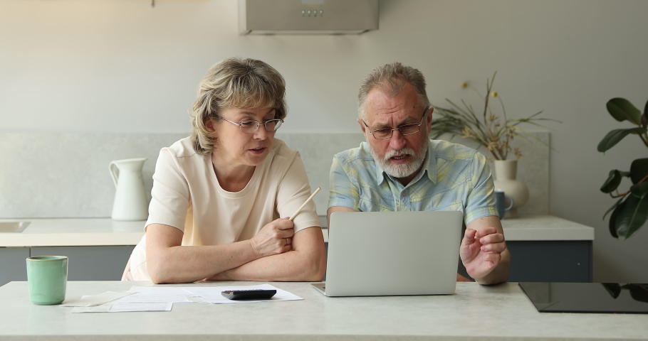 Worried aged wife comfort angry elderly husband sit by laptop deal with financial difficulties when paying bills invoices. Annoyed distressed retired couple check bank account see overspending budget Royalty-Free Stock Footage #1084126102