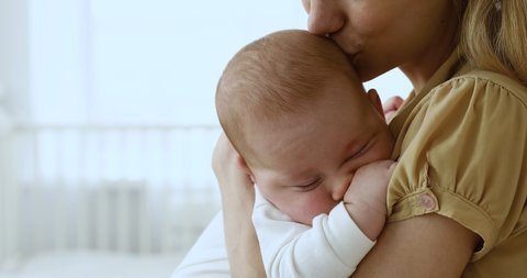 Cute infant sleeping deep on mother arms at light nursery room indoor. Happy single mom carrying small baby on hands protect serene sleep taking care of health comfort safety of little child. Close up
