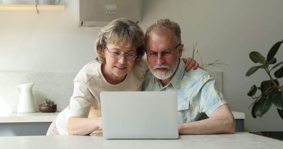 Overjoyed senior adult family couple in glasses laugh hug before pc screen getting surprise gift after winning game receiving financial reward. Excited grandparents lottery winners celebrate success Royalty-Free Stock Footage #1084126180