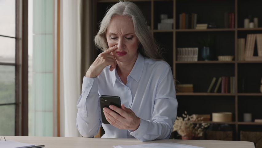 Worried old age businesswoman receive bad phone message refusal answer on cooperation offer reneging on deal breach of contract with partner. Nervous aged lady entrepreneur get bank email about debt | Shutterstock HD Video #1084126381