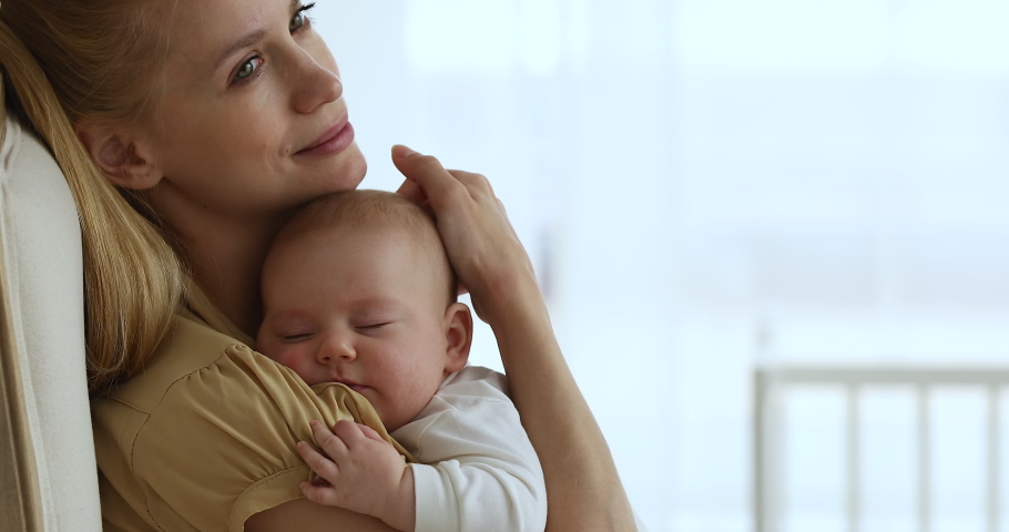 Happy serene mother sit in armchair cuddle caress tender baby napping on her shoulder look at distance dream of good health happy future for kid. Smiling relaxed mom guard sweet sleep of infant child Royalty-Free Stock Footage #1084126477