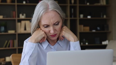 Nervous worried old age businesswoman look on laptop screen with indecision hesitate make difficult choice in risky situation. Anxious mature lady employee lost in thoughts ponder on business problem