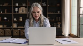 Diligent aged student. Enthusiastic senior female study online on retirement using laptop make notes check past records at copybook. Happy elderly lady enjoy receiving new skills at distant web course