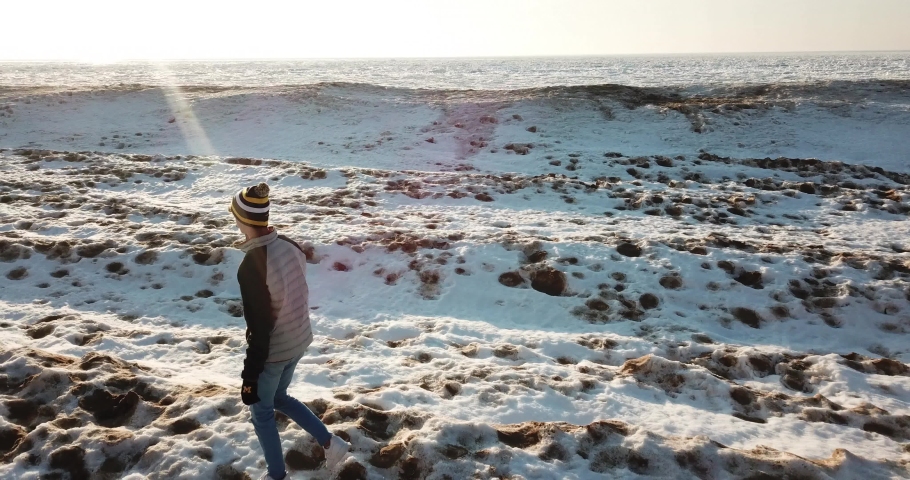 Aerial Footage of Man Walking and Running Along Shoreline of Frozen Lake with Snow Everywhere