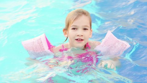time-lapse. a funny little girl swims and plays in inflatable armbands in a pool. safety of children on the water. inflatable toys for swimming and playing in the water. swimming training.