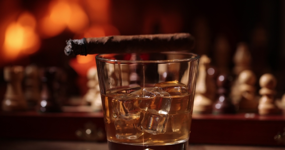 Drinks at fireplace on winter evening. Time to enjoy!   High-quality cigars and cognacs, whiskey on a wooden chess table. A flames in the background. Whiskey , chess and steaming cigar on the table in | Shutterstock HD Video #1084128748
