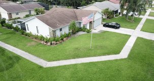 Aerial drone footage showing American flag pole in front yard of Florida house, then drone moves up and over house to reveal neighborhood and other houses.