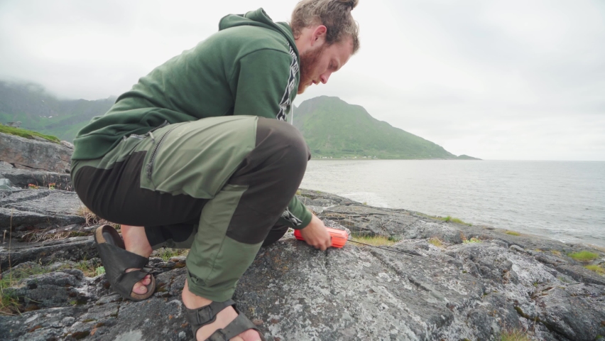 Male Hiker Preparing His Fishing Rod By The Lake of Segla Mountain In Senja Island, Norway. Medium Shot. Royalty-Free Stock Footage #1084134850