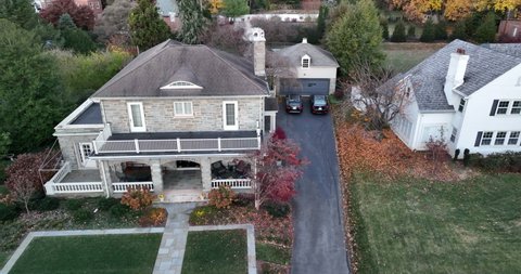 Aerial establishing shot of upscale home in USA. Cold autumn scene with slo motion smoke from chimney. Cars parked in driveway.