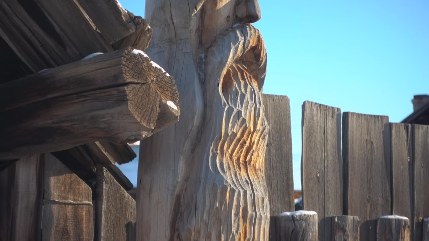 Gimbal close to ancient wooden idol carved in form of pillar. Pagan creativity Siberia Russia Buryatia. National culture heritage. Authentic village decor. Travel landmark. Blue sky, sunny winter day