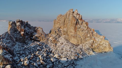 Aerial around scenic Shamanka rock, famous Buryatia sight. Winter frozen snow-capped lake Baikal natural landscape. Best Siberia travel landmark. Burkhan cape Natural monument park Blue sky. Shamanism