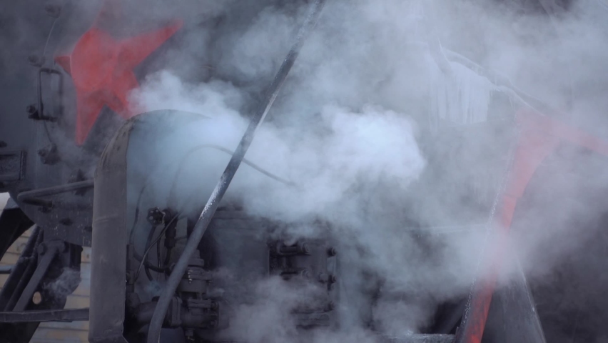 Gimbal impressive old Soviet steel locomotive, steam engine, clouds of smoke rise from mechanisms of carriages at winter in slow motion. Nose of train, first railway carriage. Siberia landmark. Travel