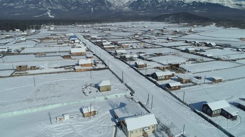 From great height Buryatia winter Arshan rural settlement, authentic wooden houses among high snow-capped mountains. Epic suburban rural landscape Baikal region Siberia. Typical Russia ancient village