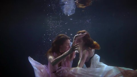 a romantic female same-sex couple swims in the dark depths of the pool, splashing and playing in dresses