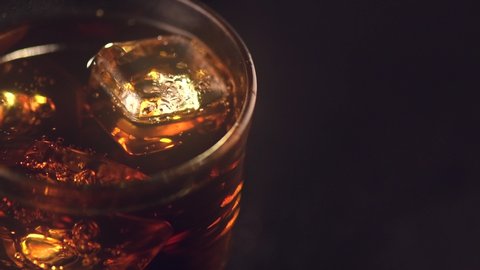 Cola with ice cubes close-up. Cola with Ice and bubbles in glass. Soda closeup. Food and drink background. Rotated glass of Cola fizzy drink over brown background. Slow motion. Top view