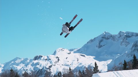 SLOW MOTION: Athletic male skier riding in the sunny Slovenian mountains takes off a kicker and does a rotating grab trick. Action shot of a freestyle skiing pro doing spectacular tricks at snowpark.