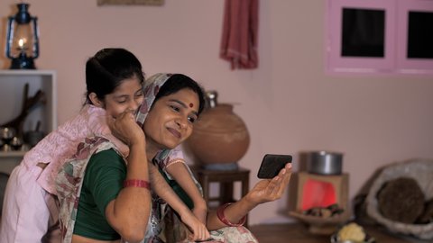 A middle-aged lady and her cute daughter of a village browsing a mobile together - Rural village home in India. A beautiful little girl and her mother spending time at home - leisure time, mother-c...