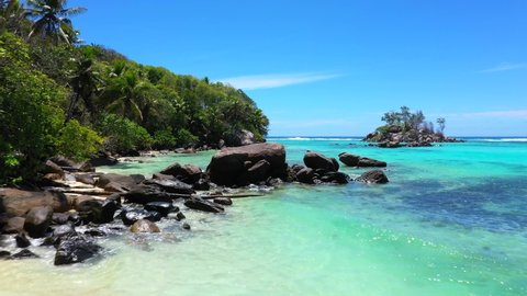 Drone clip on a beautiful beach on Mahe with turquoise blue water, rocks and palm trees in the Seychelles 