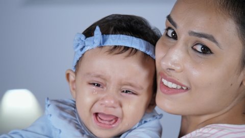 An attractive female nurse holding a little crying baby girl - Baby in tears, crying toddler. A cheerful Indian mother holding and cuddling her sweet infant - parent-child bonding, unhappy, consoli...