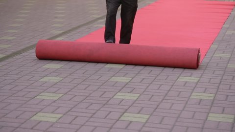 A male worker rolls out the red carpet outside for the celebration. Preparing for a festive ceremony or a party with the celebrity. Theatre or cinema awards exclusive prestige event. 