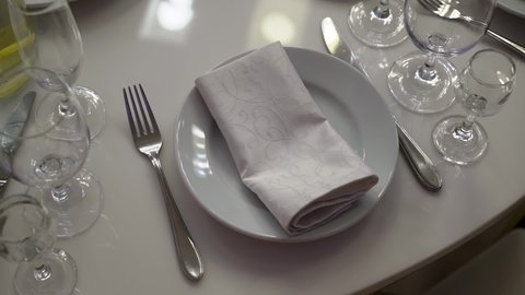 Served table in a restaurant for dinner, lunch or celebration. White tablecloth, plates, gray napkin and glasses. Holiday indoors. Empty with no people and food. Decorated for wedding