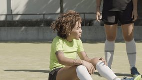 Upset woman getting hurt while playing football at stadium. Female athlete lying on ground, holding onto injured leg, crying in pain. Friends trying to help soccer team player. Sport, injury concept - Powered by Shutterstock - Get 15% off with code: PIKWIZARD15
