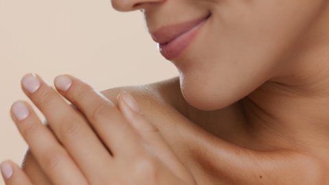 Horizontal extreme close-up of good-looking slim woman strokes her shoulder smiling on beige background  Skin nourishing concept