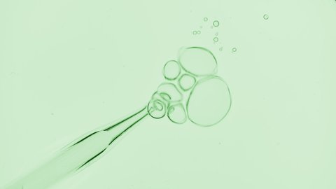 Top view macro shot of air bubbles comes out from lab dropper and float on the surface of a transparent liquid bursting on green background  Abstract cosmetics formulating concept