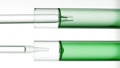 Lab dropper takes green liquid from test tube and drips it back in front of another test tube with green liquid and dropper on white background  Abstract face care cosmetics formulation concept