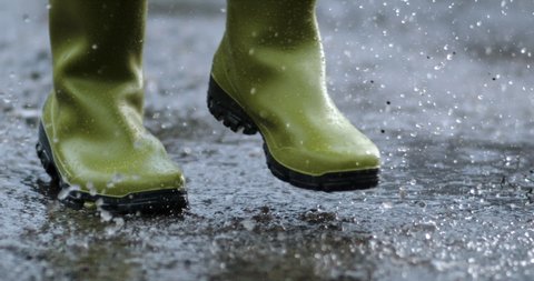 slow motion of man with a pair of boots running in a puddles during a rainy day