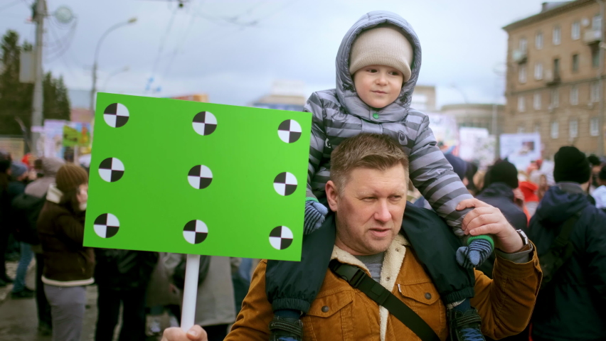 Family of protesting father and son with chroma key space banner. People at political picket demonstration on city streets. Activists with green screen mock up placard. Parent and kid at rally riot. Royalty-Free Stock Footage #1084162795