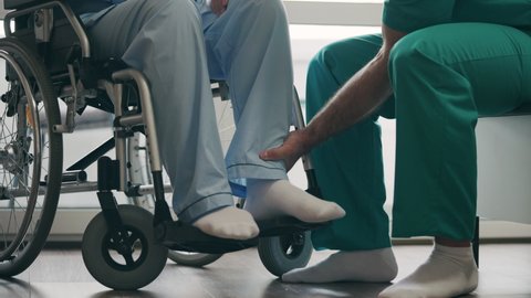 Physician examining injured patient in wheelchair, exercising after surgery