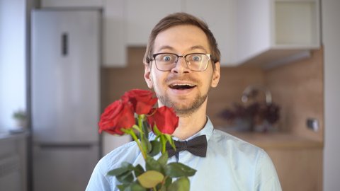 Passionate young male nerd in glasses and elegant outfit with bow tie holding red rose and looking at camera. Valentine's day concept.