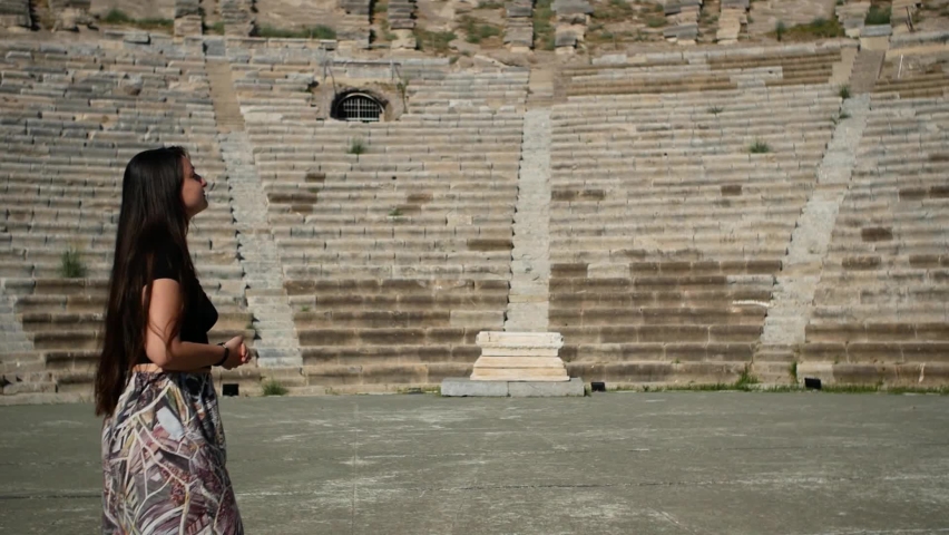 Female tourist with long brunette hair looks around in the empty old amphitheatre in Bodrum, Turkey, (Halicarnassus). Rear view. Bird flies by. Travel in Covid-19 time. Social distancing. Excursion. 