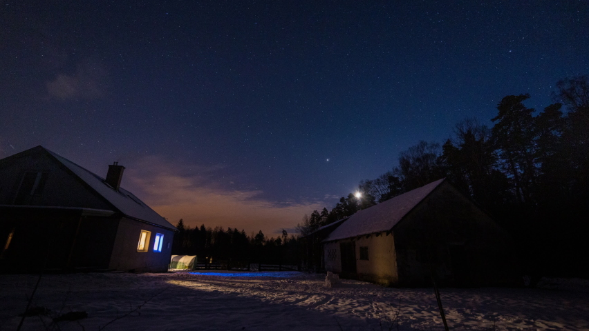 Night starry and cloudy sky over house and snowed backyard.
