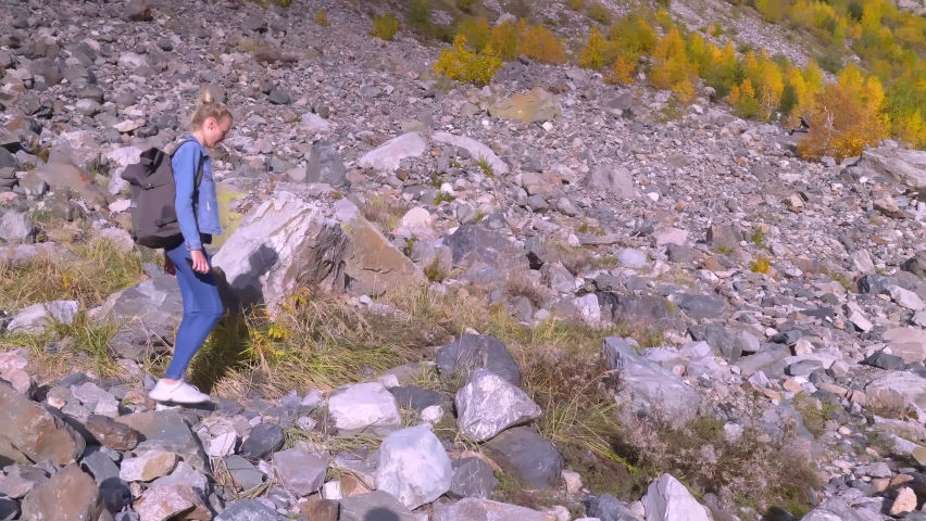 A young beautiful slender woman alone in the mountains. She walks in a denim jacket and jeans and enjoys the beautiful scenery of the highlands in autumn. Hiking. Georgia. A lonely journey.