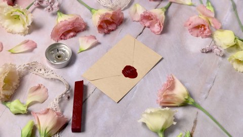 Hands taking wax sealed envelope from a marble table near pink flowers close up 
