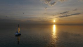 4K Video. Colorful sunset above the sea surface with sail boats, aerial view. Reflected sun on a water surface. Sunset over ocean. Seascape, Summer and travel vacation concept. 