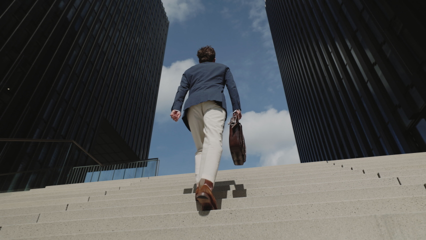 Low angle view of successful business person in formal clothes carrying suitcase while walking up on outdoor stairs. Concept of people, business and lifestyles.