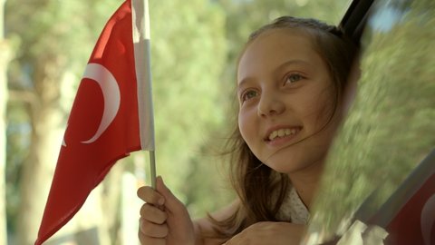 Slow Motion:Beautiful little girl waving Turkish flag out of a car window.Travel Concept. Little girl coming out of the car window smiling and waving the Turkish flag. Celebration concept. 