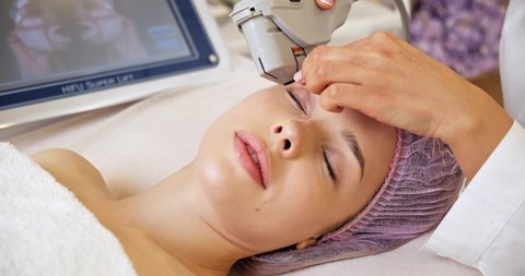 Woman in a spa salon on cosmetic procedures for facial care. Cosmetologist making a woman a therapeutic laser processing on a face. Beautician makes laser therapy on a female face.
