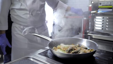 Close-up.A professional chef prepares seafood in the flambe style. Cooking a dish on fire.The cook cooks by tossing food on the fire on the gas stove in the kitchen.Fine cuisine in an elite restaurant