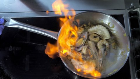 Close-up.A professional chef prepares seafood in the flambe style. Cooking a dish on fire.The cook cooks by tossing food on the fire on the gas stove in the kitchen.Fine cuisine in an elite restaurant