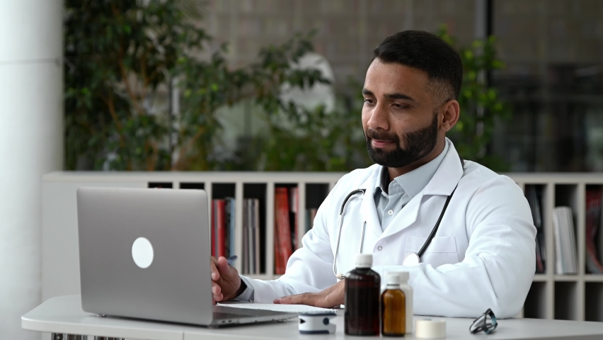 Proud smart Indian doctor therapist conducts an online consultation. Male doctor communicates with his patient by video call using laptop, prescribes treatment, answers questions,makes recommendations