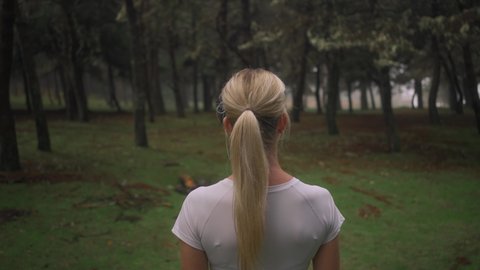Behind lost fit woman standing in mysterious forest, looking at enchanted woods