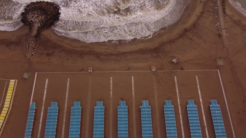 Aerial top down of colorful tents of spa resort at sandy beside crashing waves of Ocean - Mar del Plata,Argentina - Ascending drone shot