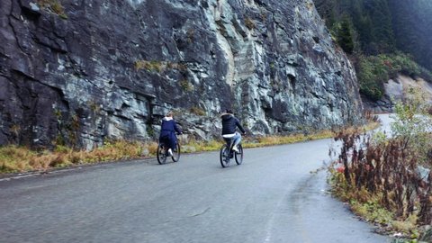 Aerial shot of man and woman cycling on the asphalt road in mountains. Travel by bicycle. Outdoor activities concept. 4k.