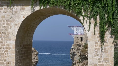 Polignano a Mare , Italy - 09 18 2021: Red Bull Cliff Diving board seen through Roman arch.